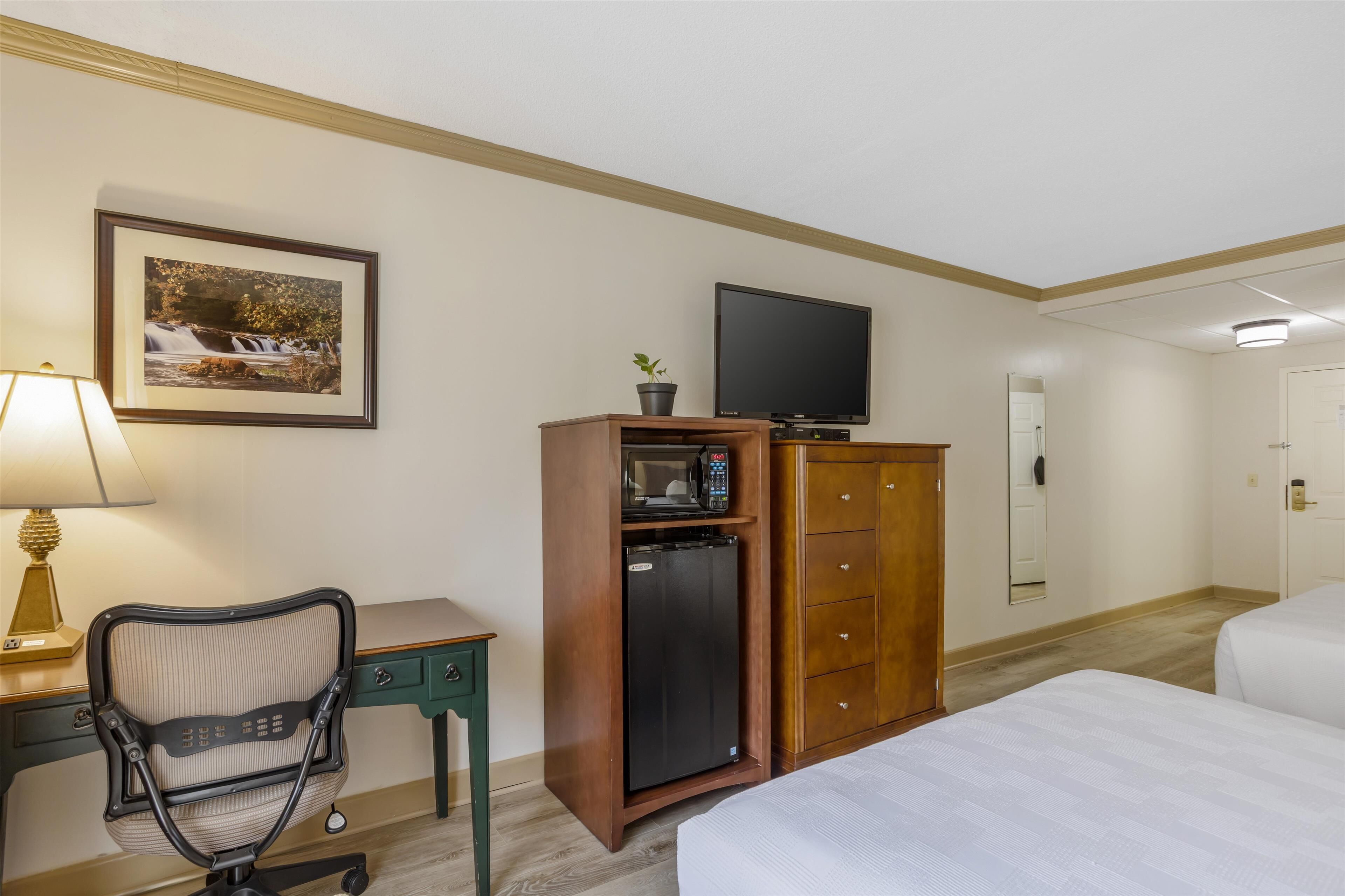 Una habitación de hotel con una cama, un escritorio con silla, un televisor, un refrigerador y un armario.
