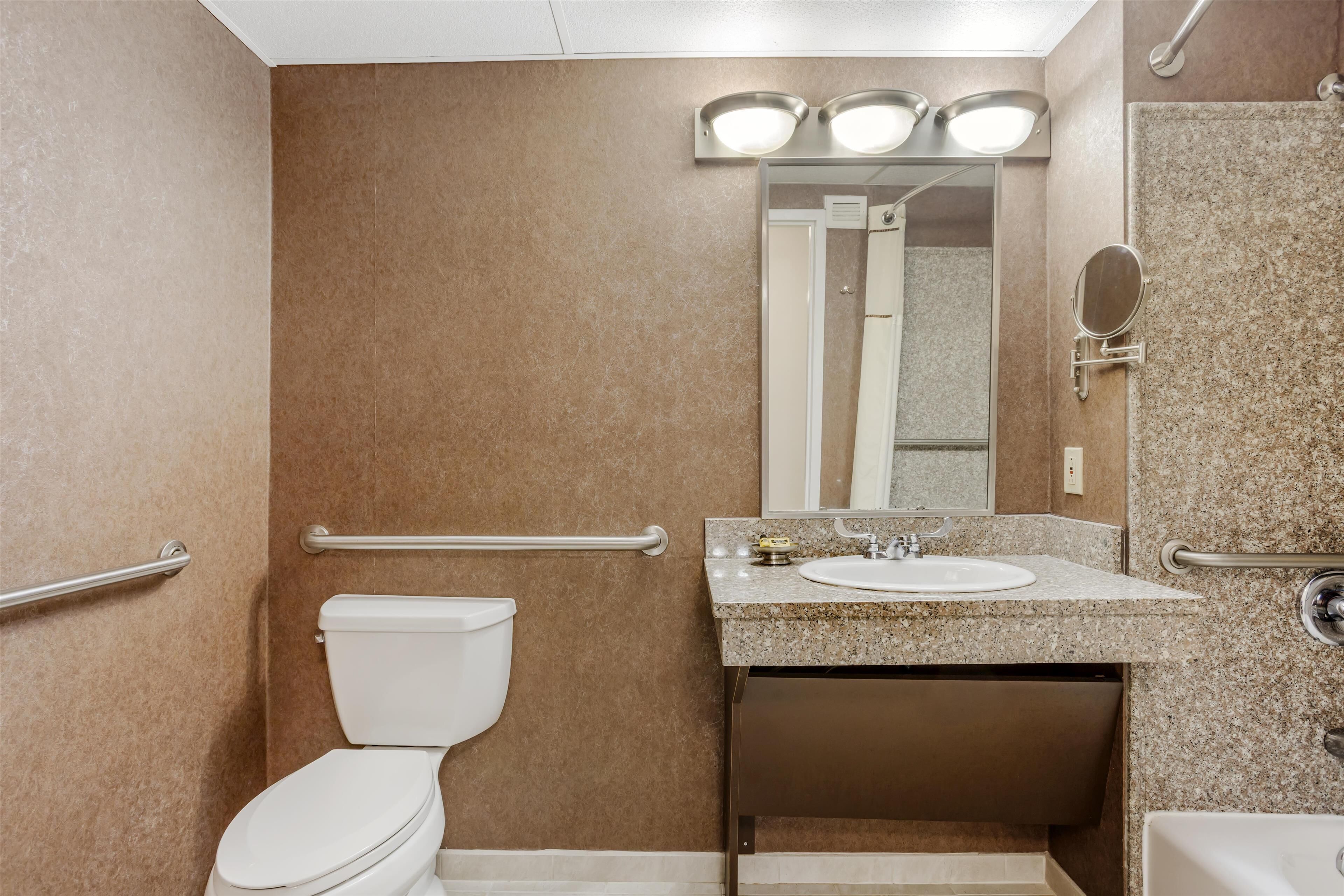 A bathroom with a toilet, sink, mirror, and shower.