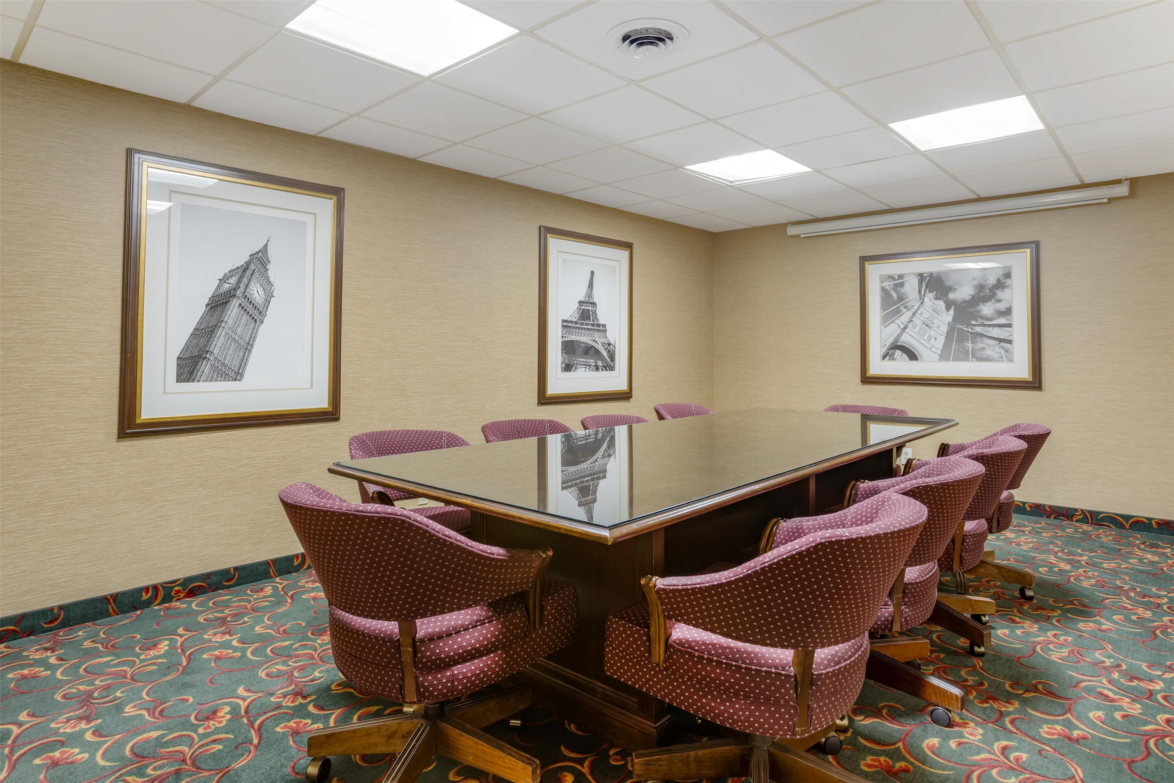 A conference room with a glass table, six chairs, and framed pictures of famous landmarks on the walls.