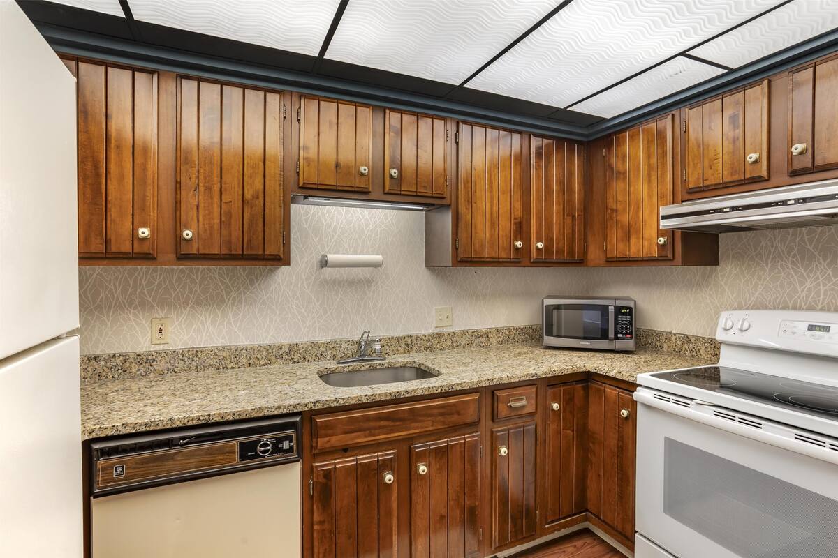A kitchen with wooden cabinets, a granite countertop, a built-in microwave, and a dishwasher.