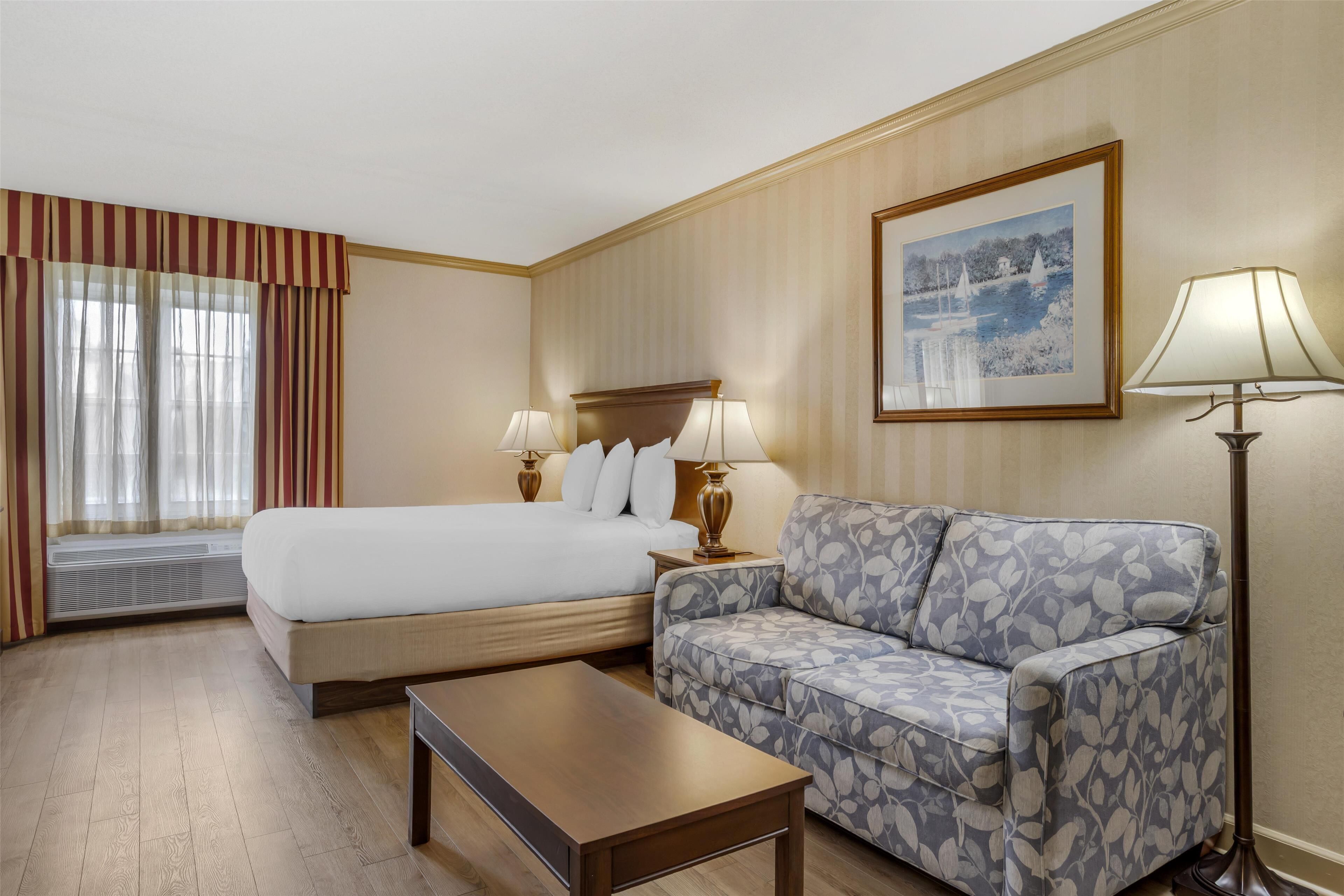 A hotel room with a large bed, a sofa, a coffee table, and a picture on the wall.