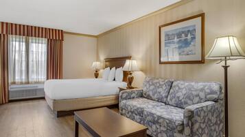 A hotel room with a large bed, a sofa, a coffee table, and a picture on the wall.