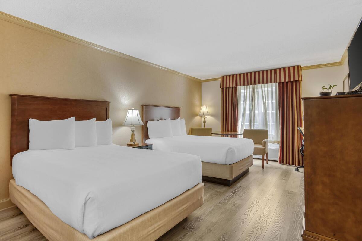 A hotel room with two beds, a desk, a chair, and a TV.