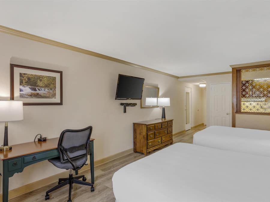 A hotel room with a bed, a desk with a chair, a dresser, a television, and a framed picture on the wall.