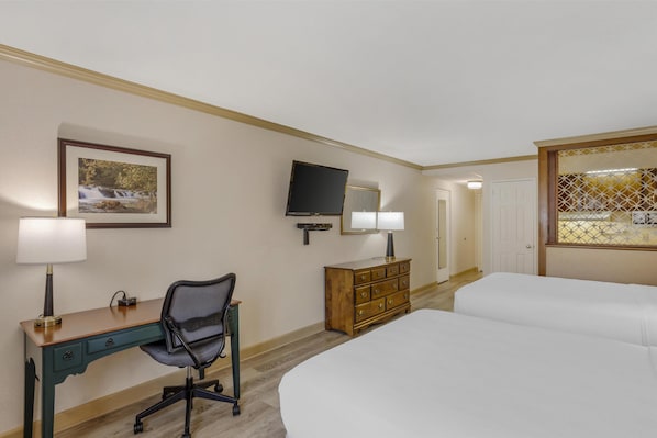 Ein Hotelzimmer mit einem Bett, einem Schreibtisch mit Stuhl, einem Schminktisch, einem Fernseher und einem gerahmten Bild an der Wand.