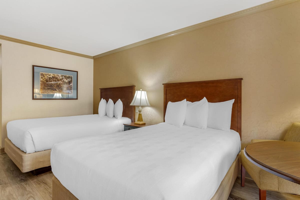 A hotel room with two beds, a wooden headboard, a small table, and a lamp.