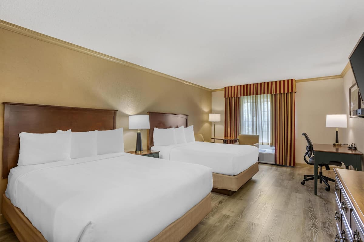 A hotel room with two beds, a desk, a chair, and a TV.
