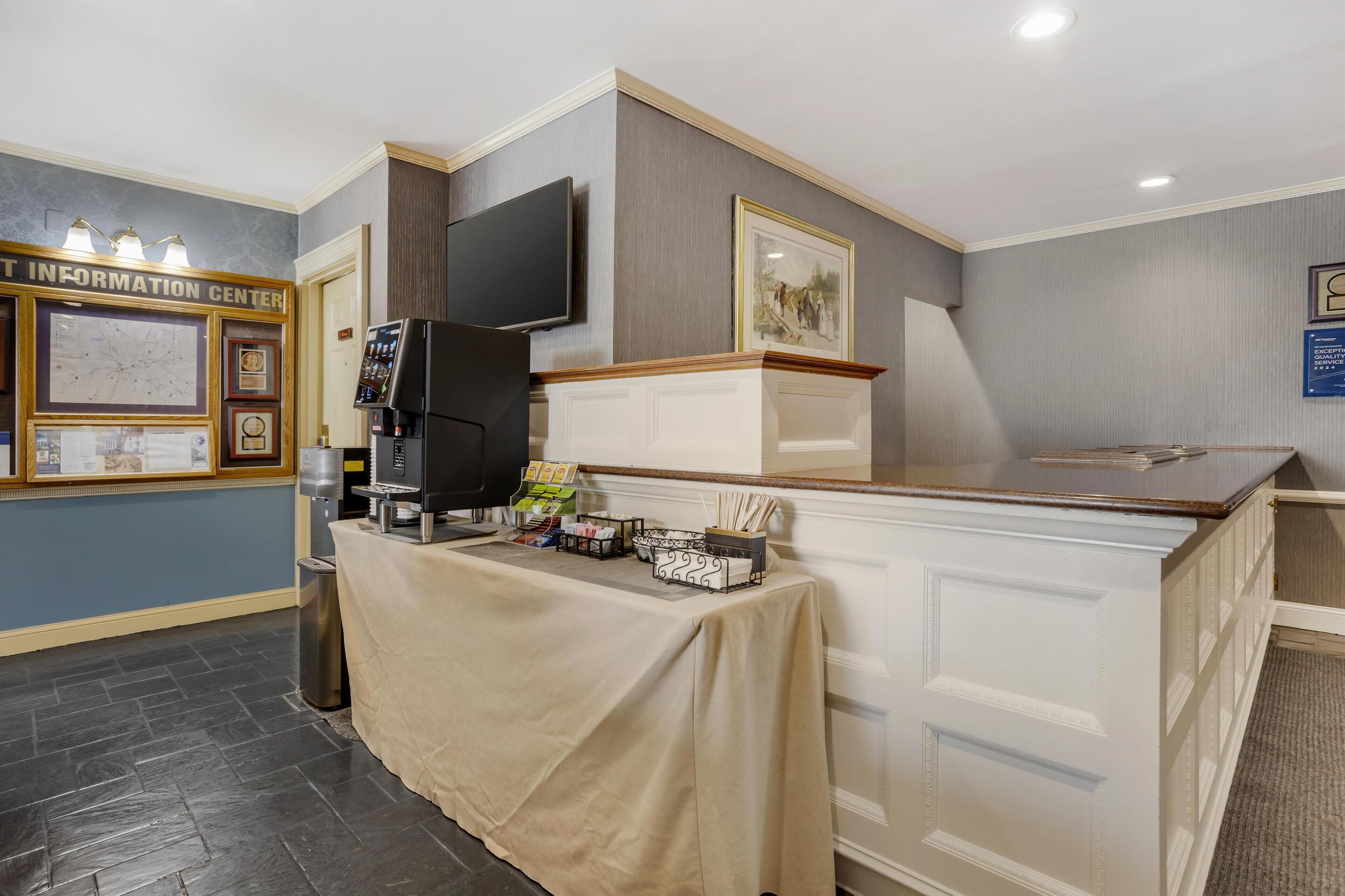 A reception area with a counter, a coffee machine, a TV, framed pictures, and a map on the wall.