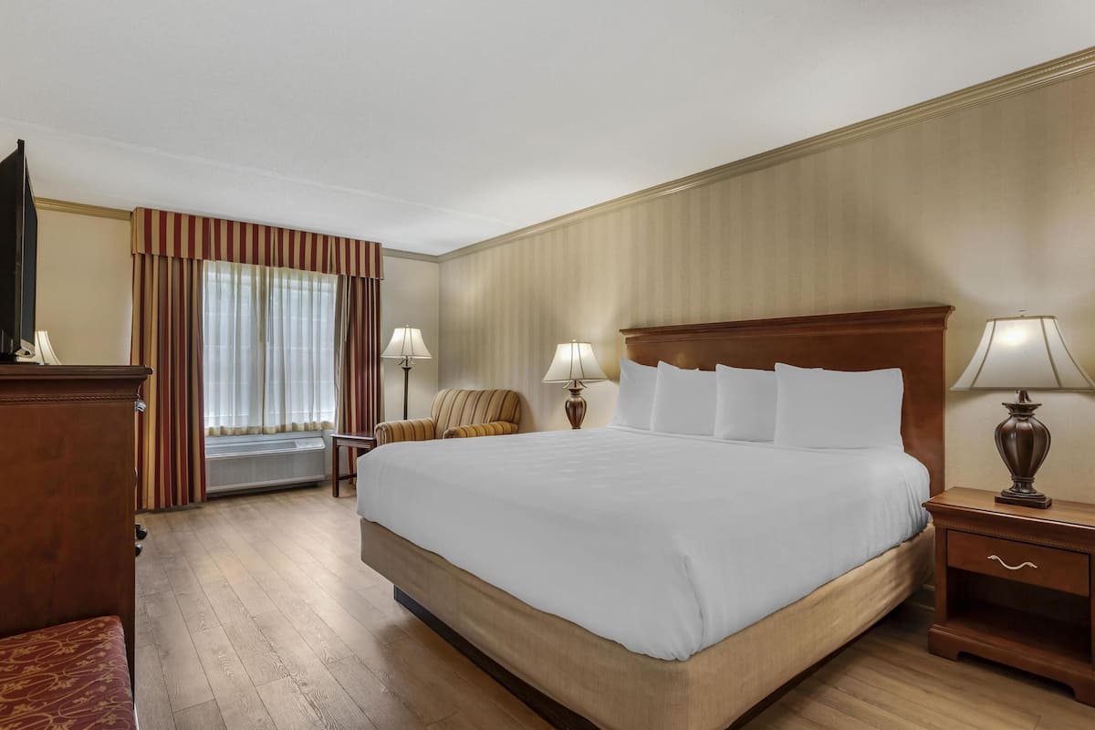 A hotel room with a large bed, two bedside tables with lamps, a chair, a desk, and a window with curtains.