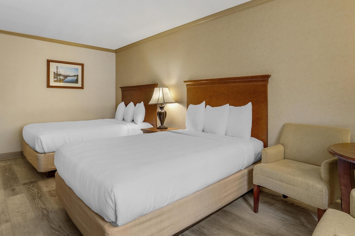 A hotel room with two beds, a sofa, a lamp, and a framed picture on the wall.