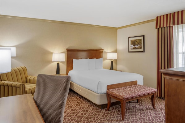 A hotel room with a bed, two bedside lamps, a chair, a bench, and a desk.