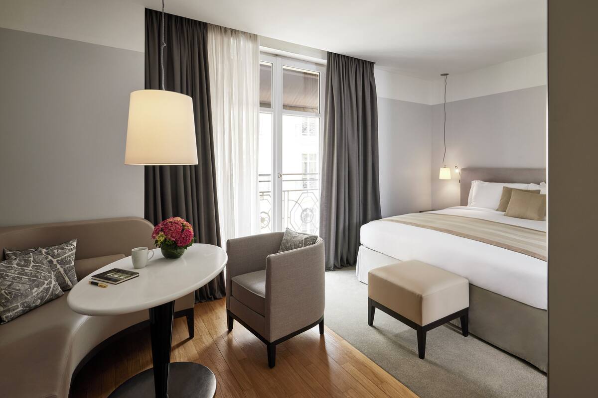 Una habitación de hotel con cama, sofá, sillón, una mesita y una lámpara.