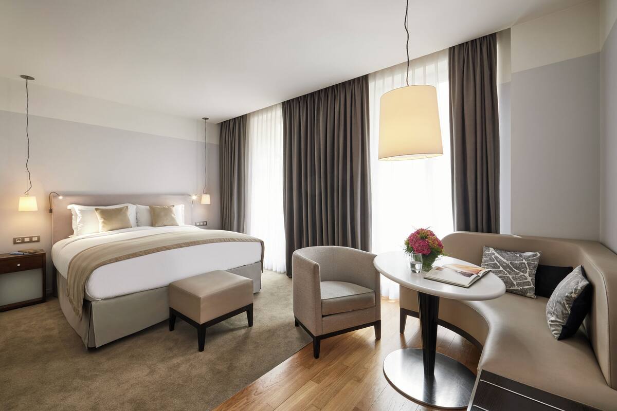 Una habitación de hotel moderna con una cama grande, un sofá, una mesita y una silla.