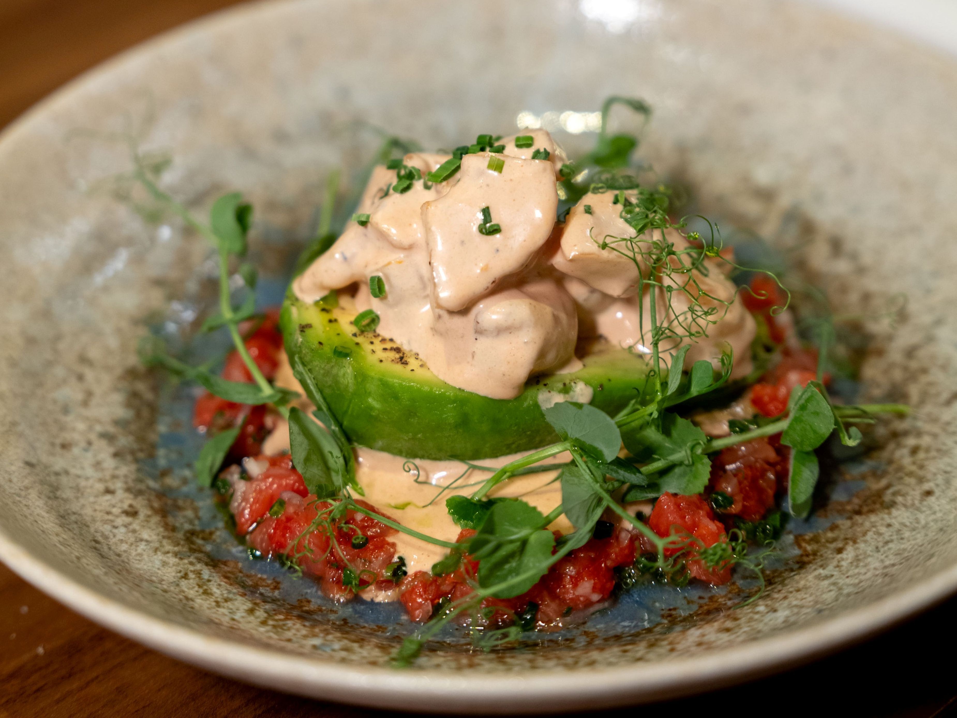 Een bord met avocado, een romige saus en verse groenten.