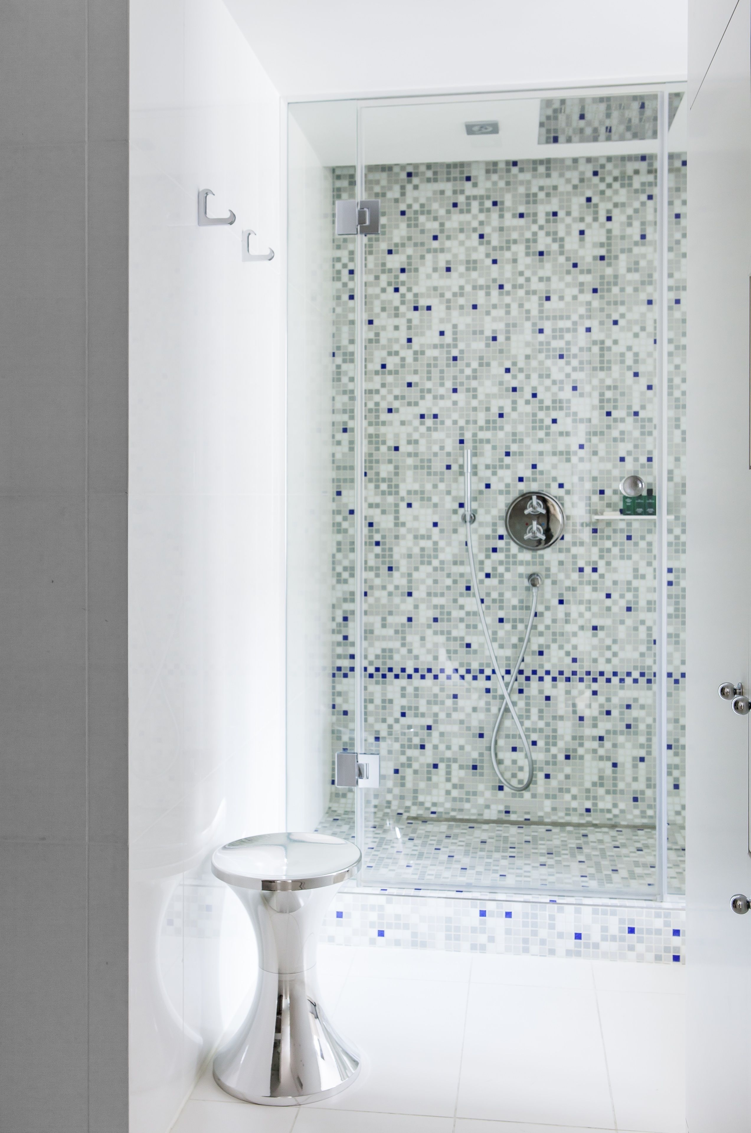 Une salle de bain moderne avec une douche à parois de verre, une petite table ronde et un mur recouvert d’une mosaïque.