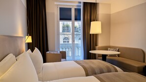 A hotel room with a bed, a sofa, a small table, and a view of a building through a window. - Sofitel Paris Arc de Triomphe (Paris)