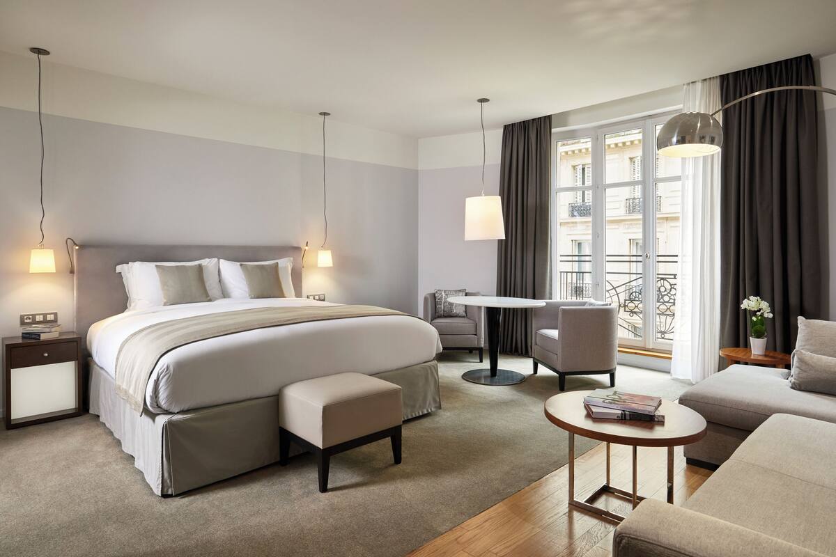 Una habitación de hotel moderna con una cama grande, una mesita, un sofá y un balcón con vistas.