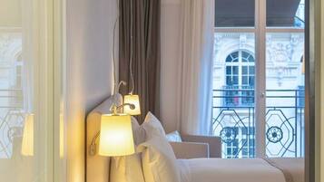 Une chambre d’hôtel avec un lit, une table de chevet avec une télécommande et une fenêtre donnant sur un immeuble.