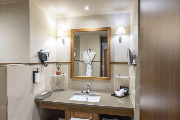 A hotel bathroom with a sink, mirror, robe, towel rack, and toiletries.