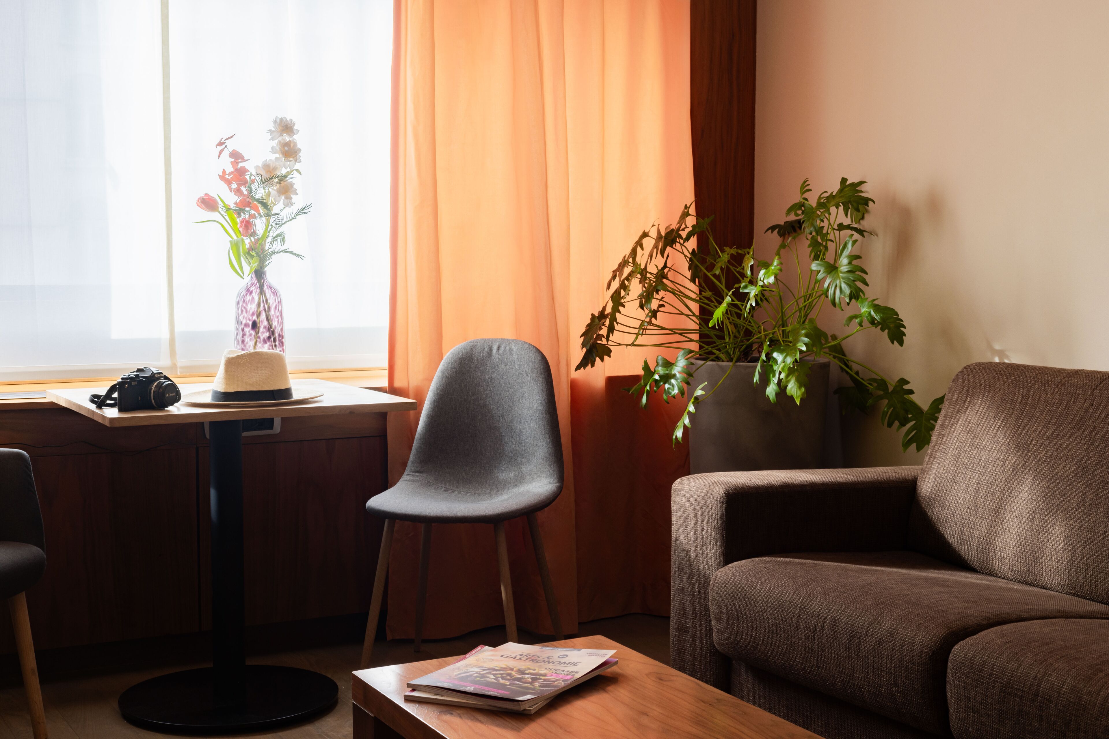 A room with a wooden desk, a grey chair, a brown sofa, and a potted plant.