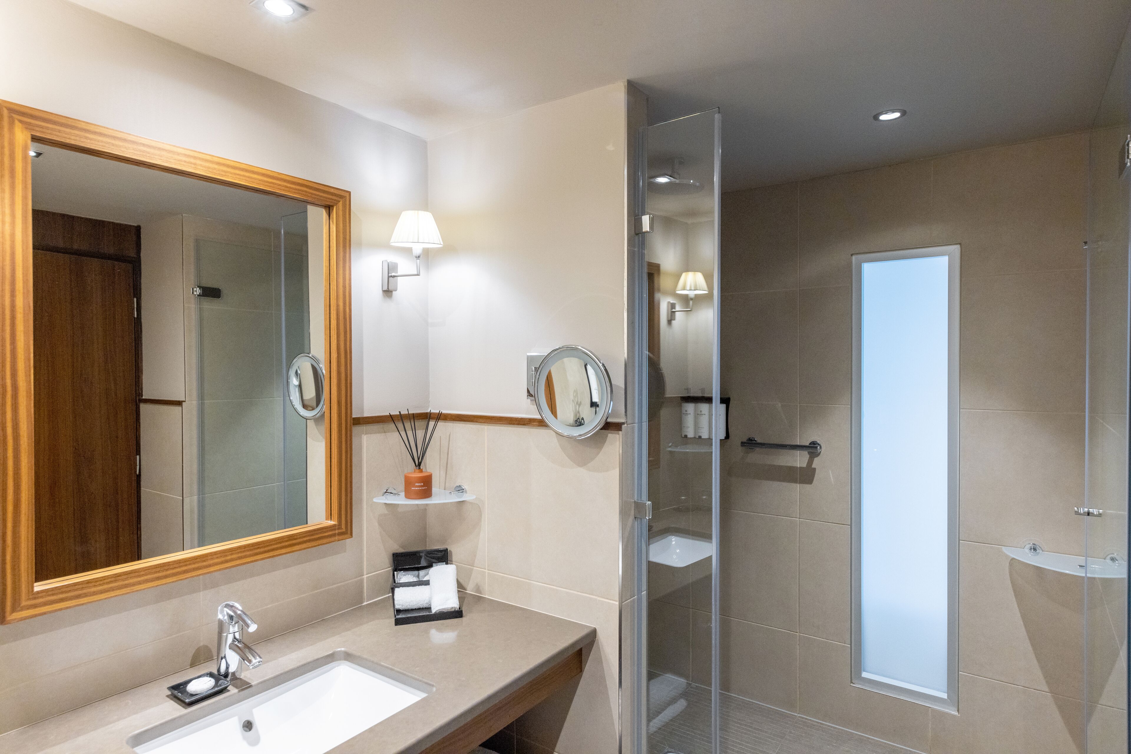 A modern bathroom with a large mirror, a sink, a glass shower enclosure, and a towel rack.