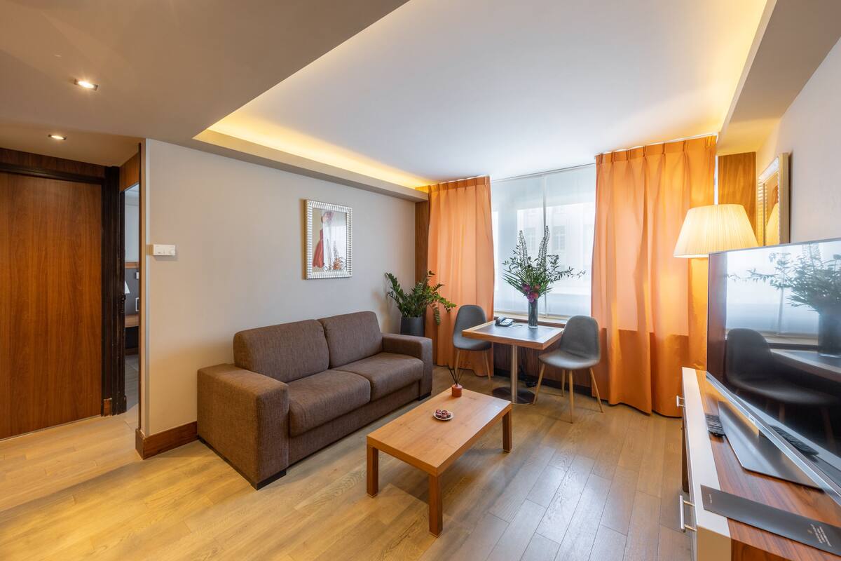Een moderne woonkamer met een bank, salontafel en televisie. Er is een eethoek met een tafel en stoelen.