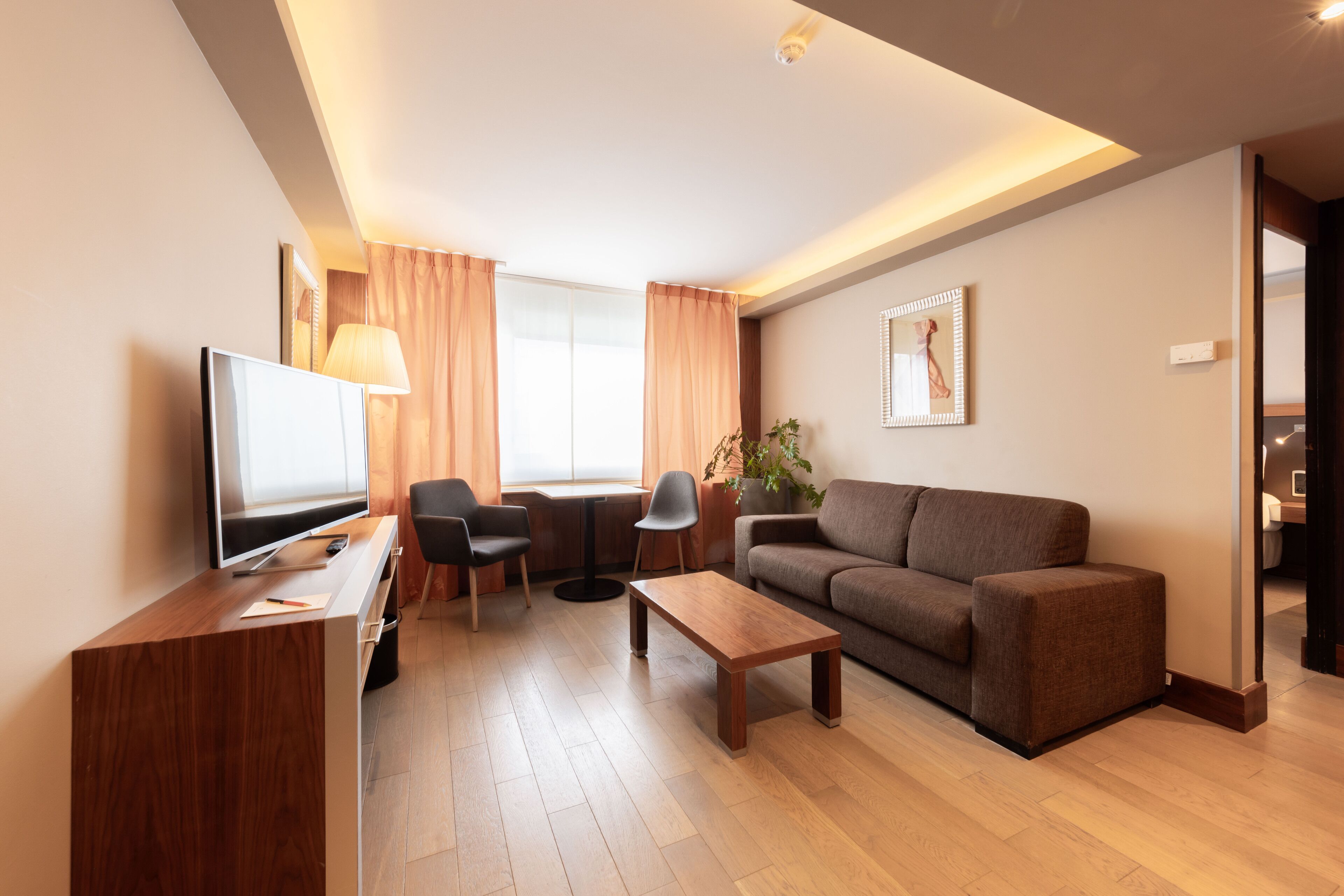 Una sala de estar moderna con televisor de pantalla plana, una mesa de centro de madera, un sofá marrón y una zona de comedor con mesa y sillas.