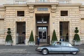 The entrance of the Hôtel de Crillon with a classic stone facade, double doors, and a car parked in front.