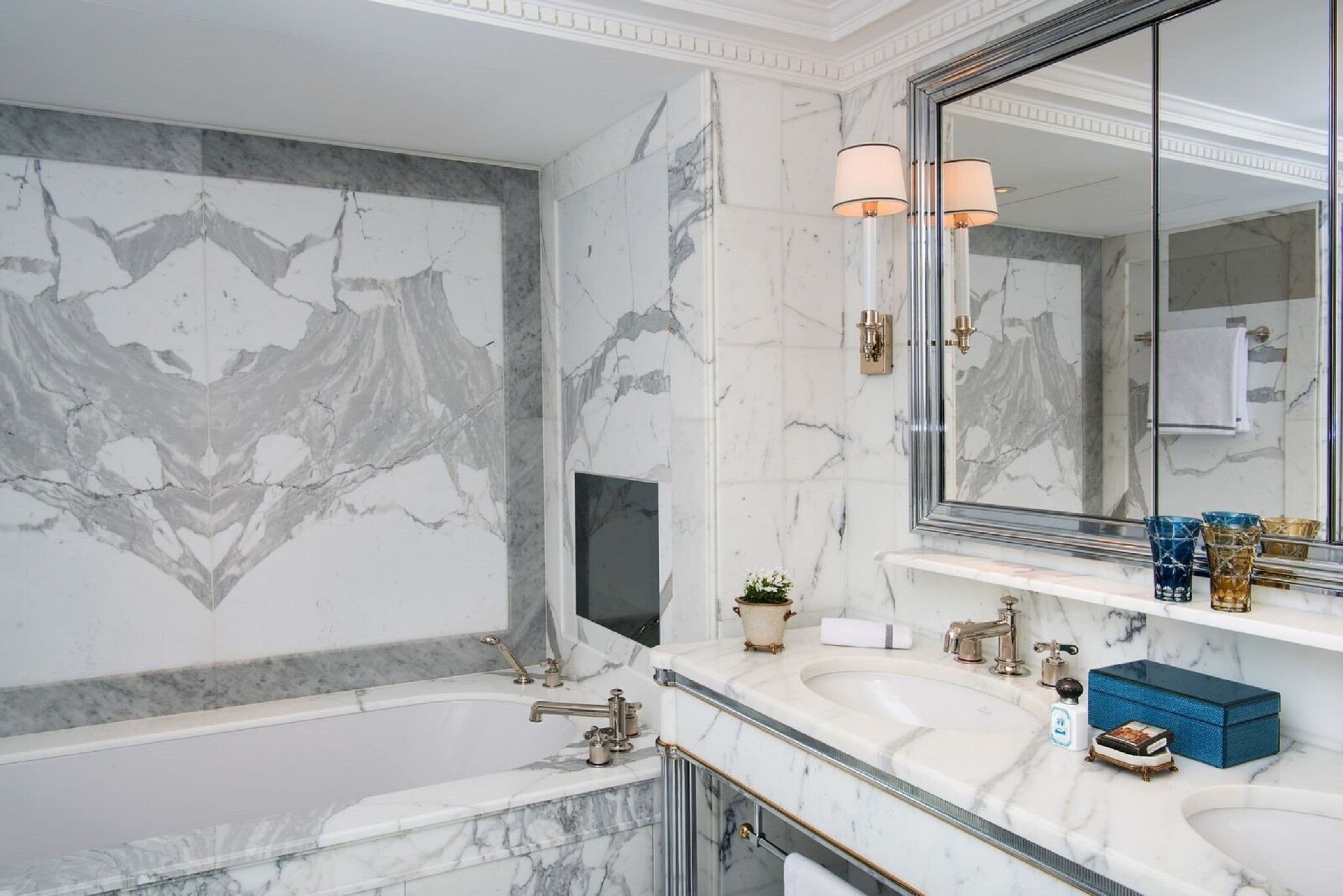 A bathroom with marble walls, a large mirror, two sinks, and a bathtub.