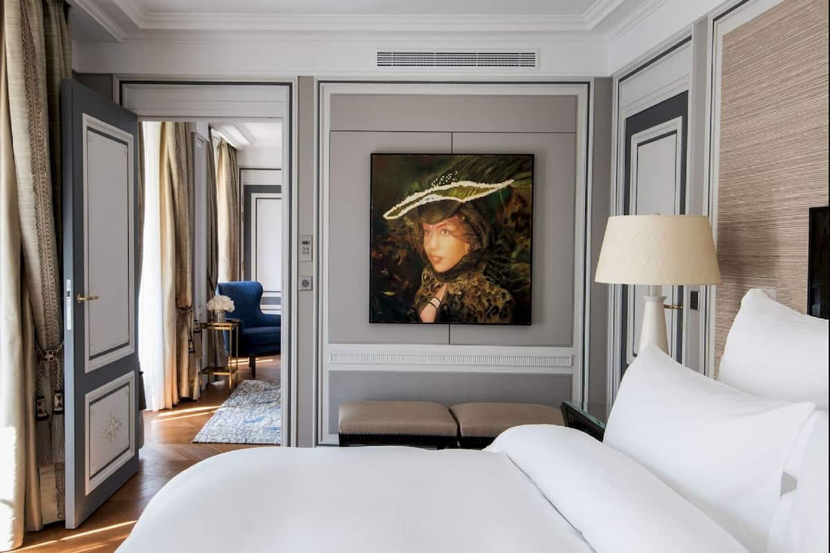 Une chambre d’hôtel avec un grand lit, un téléviseur fixé au mur, une table de chevet avec une lampe et une vue sur le couloir.