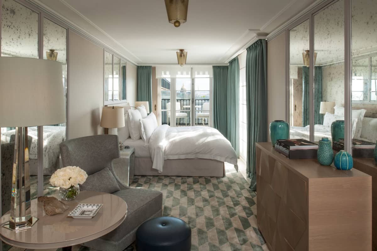 Une chambre d’hôtel comprenant un lit, un coin salon avec une table, une commode et un grand miroir.