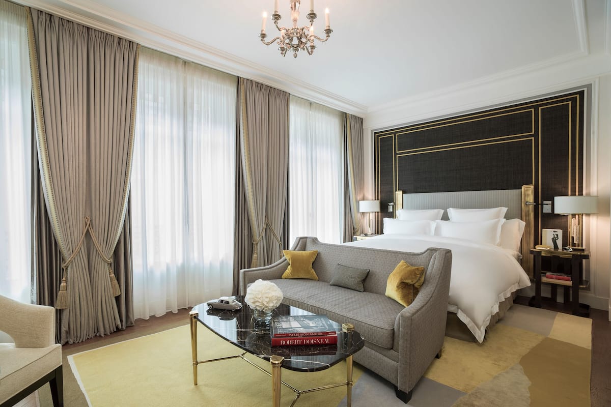 Une chambre d’hôtel avec un grand lit, un canapé, une table basse et un lustre.