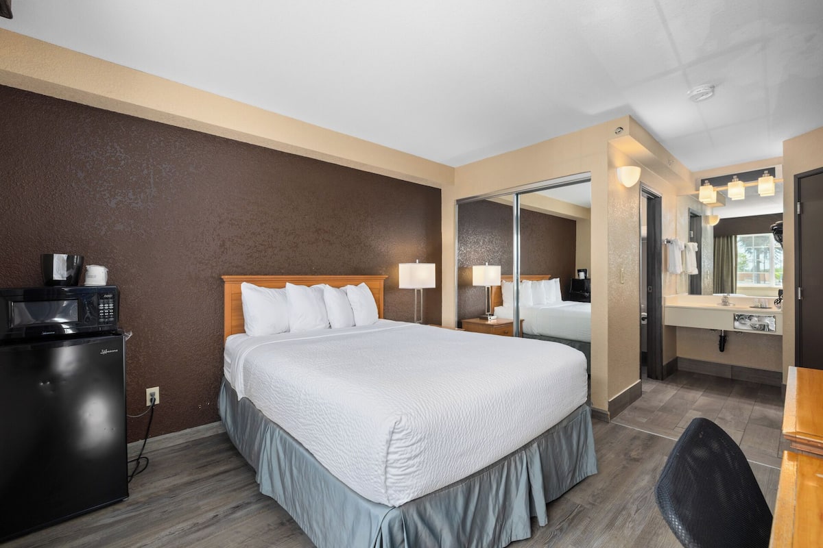 Ein Hotelzimmer mit Bett, Schreibtisch mit Mikrowelle, Spiegel und Bad mit Waschbecken und Spiegel.