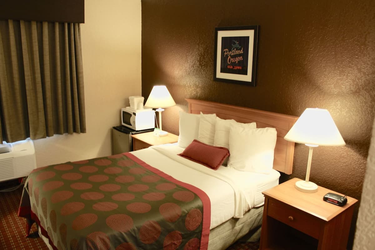 Ein Hotelzimmer mit einem Bett, zwei Nachttischen, einem an der Wand befestigten Fernseher und einem gerahmten Schild.