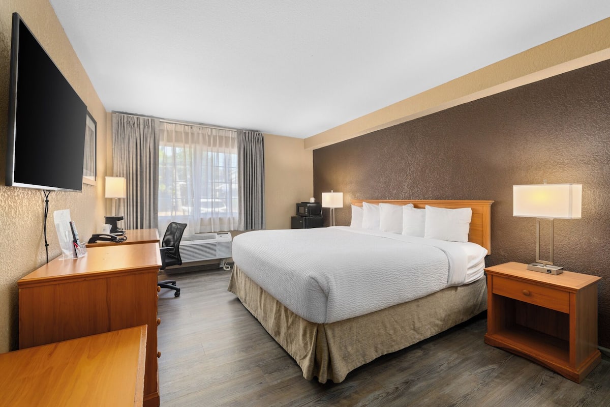 Ein Hotelzimmer mit einem großen Bett, Nachttischen, einem Schreibtisch, einem Flachbildfernseher und einem Fenster mit Vorhängen.