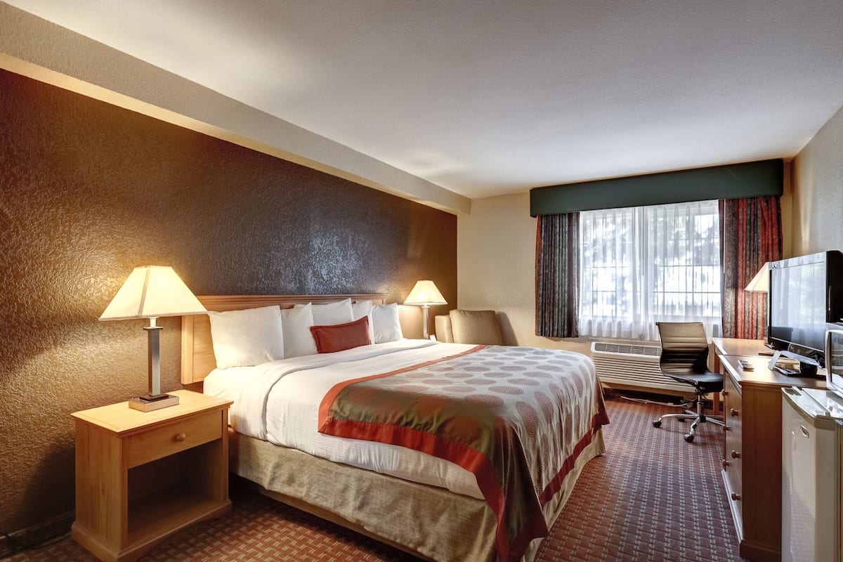 Ein Hotelzimmer mit Bett, Nachttischen, einem Schreibtisch mit Stuhl, einem Fernseher und einem Fenster mit Vorhängen.