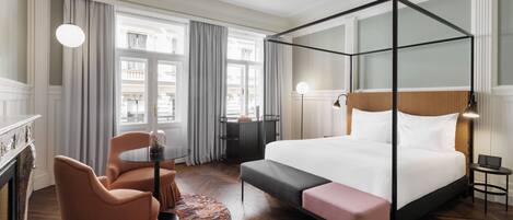 Quarto de hotel moderno com uma cama de dossel, uma mesa redonda com cadeiras, lareira e vista para a cidade.
