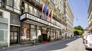 Fachada de hotel de estilo arquitectónico clásico, con amplias ventanas, alfombra roja en la entrada y varias banderas.