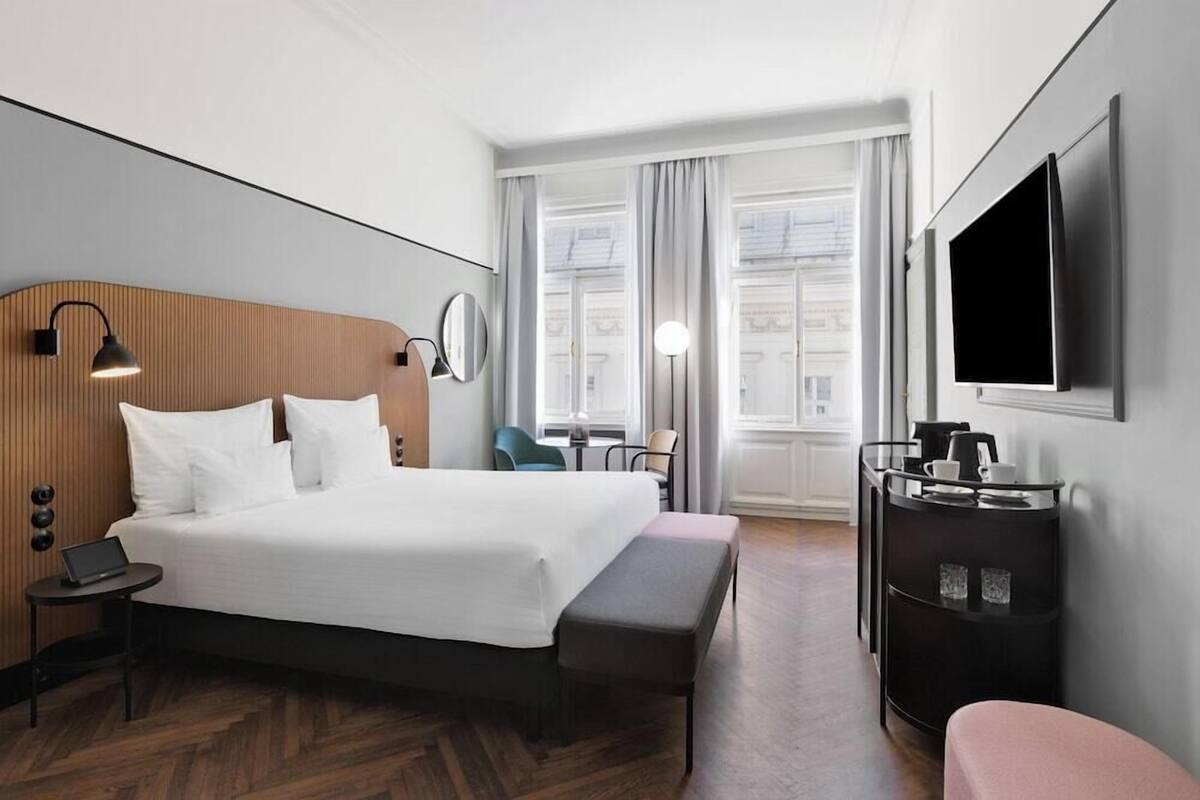 A hotel room with a large bed, bedside table, lamp, TV, and a small desk with a chair.