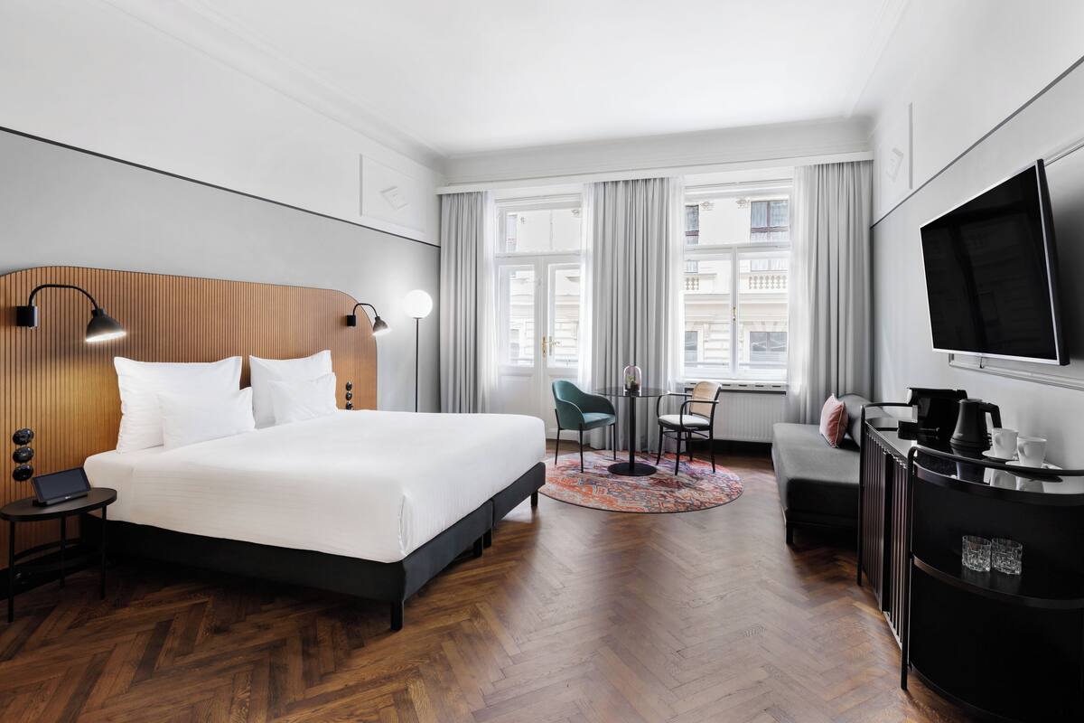 A modern hotel room with a large bed, a desk, a chair, a sofa, and a TV.