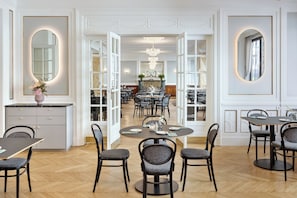 A spacious dining area with round tables and chairs, a chandelier, and a view into the dining room. - Hotel Astoria Vienna, Curio Collection by Hilton (Vienna)