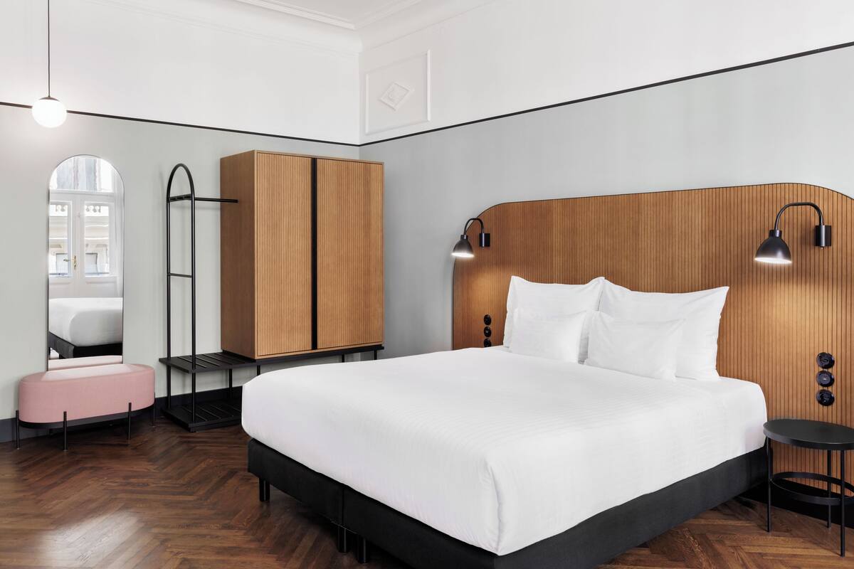A modern bedroom with a large bed, wooden wardrobe, and a mirror.