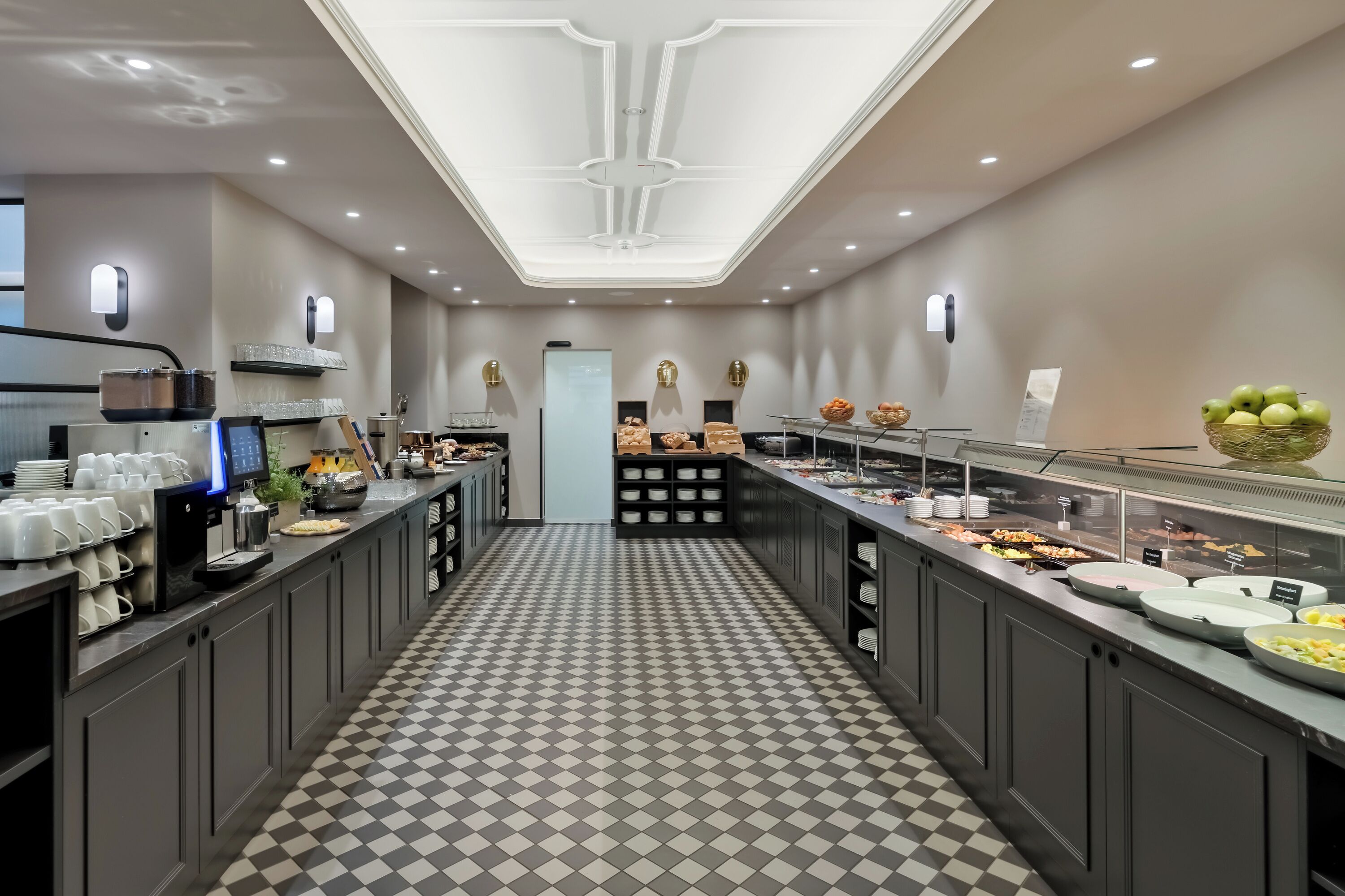 Una cocina moderna con suelo a cuadros, una estación de café y diferentes vitrinas con alimentos.