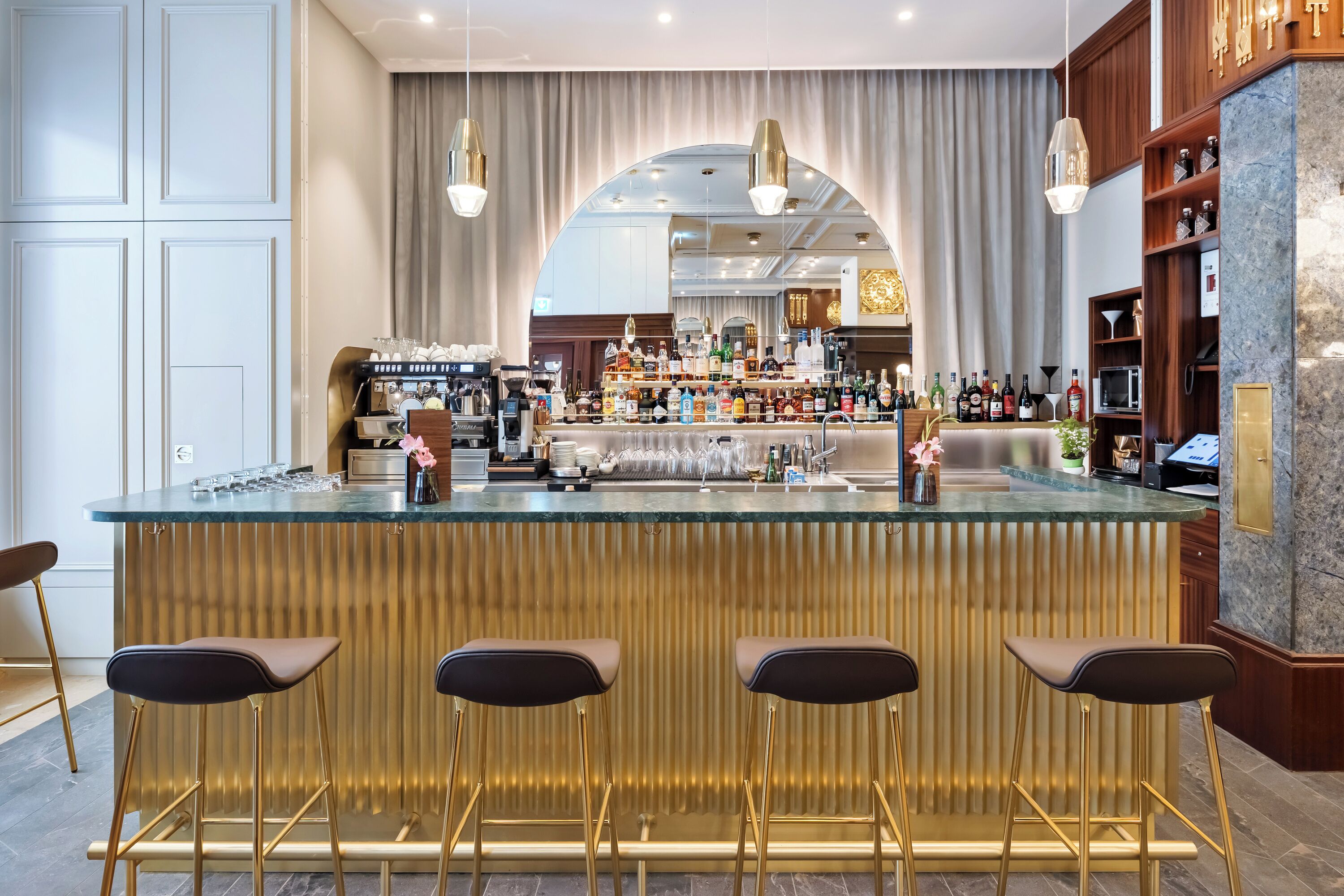A bar area with a glass countertop, bar stools, and a variety of bottles and glasses.