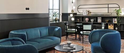 Un área de estar moderna con un sofá azul, sillones, una mesa redonda de centro y una alfombra estampada.