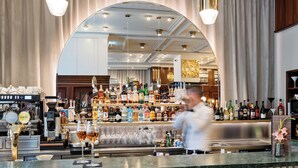 Una zona de bar con mostrador, diferentes botellas, copas y un cocinero preparando comida.