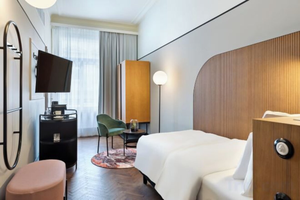 A hotel room with a bed, a desk with a computer, a chair, a television, and a large window with curtains.