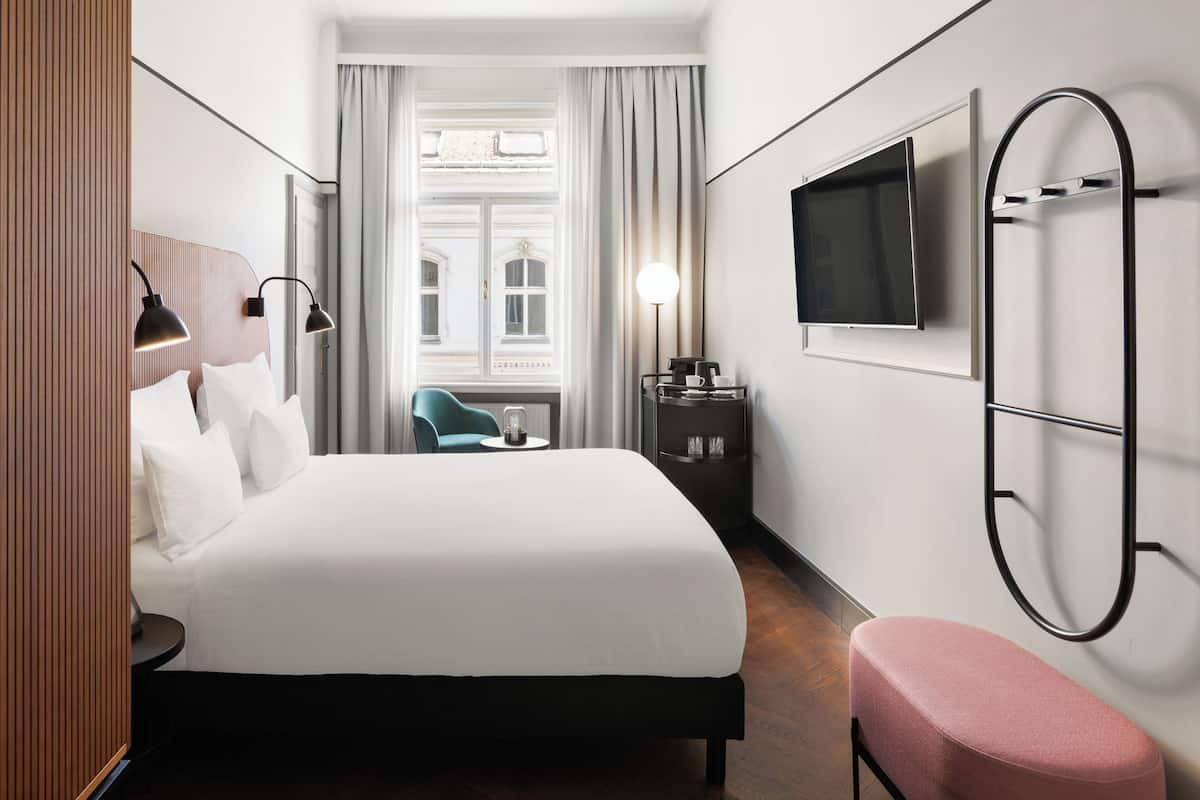 A hotel room with a bed, a desk, a chair, a TV, and a window with curtains.