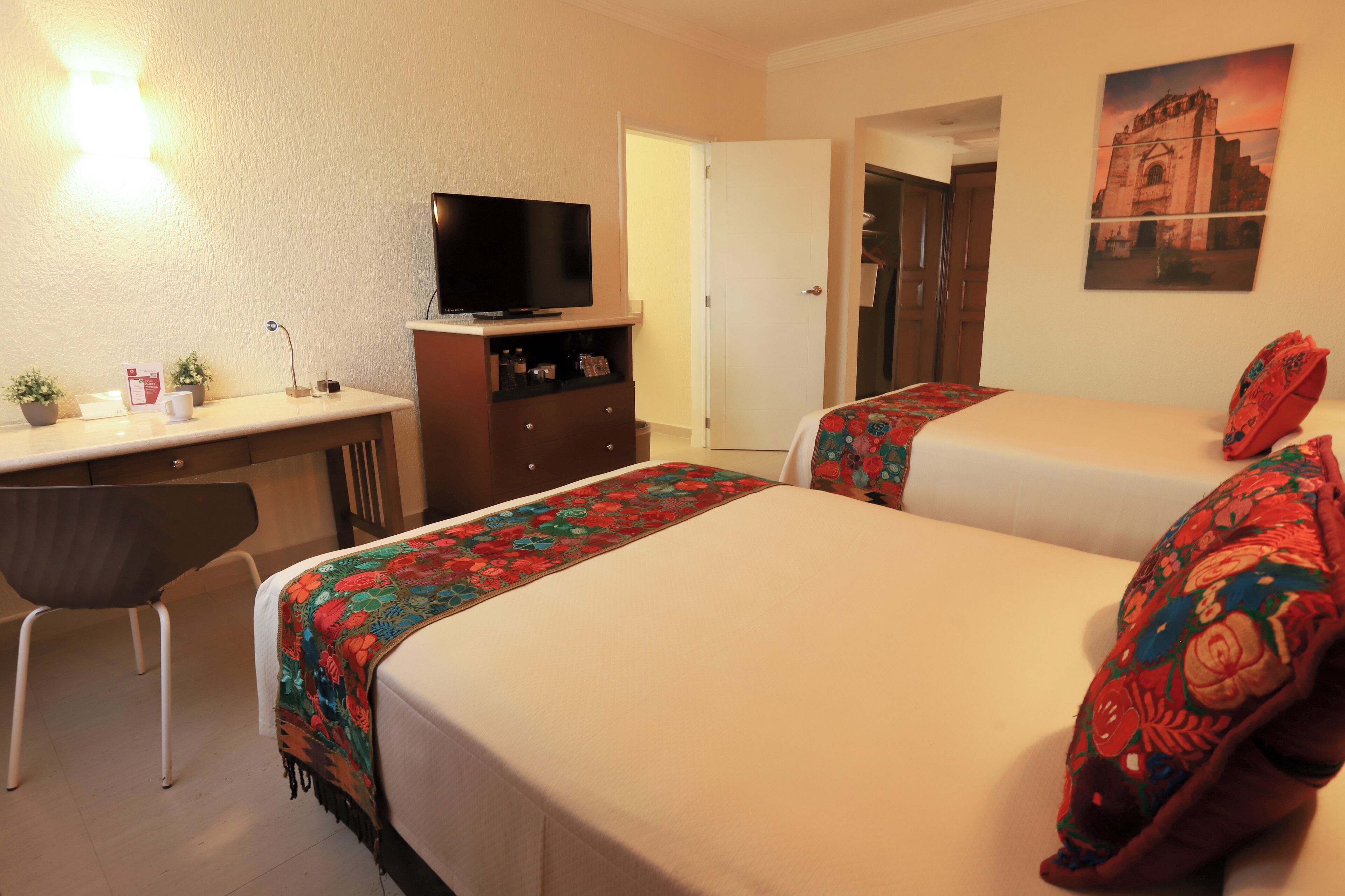 Ein Hotelzimmer mit zwei Betten, einem Schreibtisch, einem Fernseher und einer Tür zu einem weiteren Raum.
