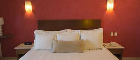 Habitación de hotel con una cama grande, dos mesitas de noche y dos lámparas de pared.